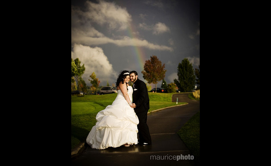 Bride and groom pose in front of a rainbow at Newcastle Golf Club.