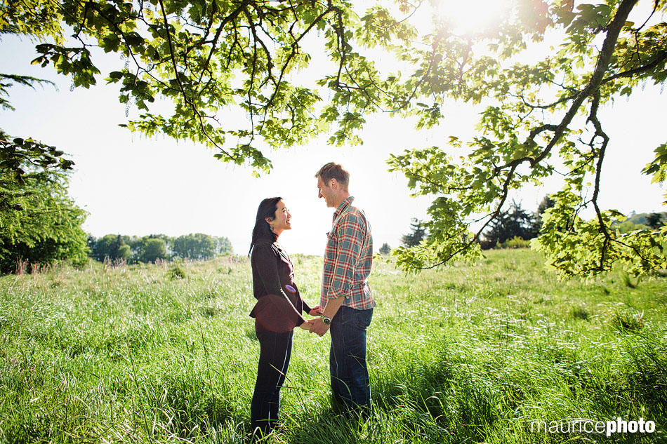 A couple pose for engagement photos before sunset under a tree at Discovery Park. 